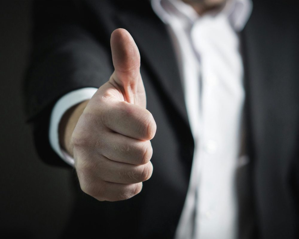 A close-up of a man's thumbs up gesture, symbolizing success and agreement.